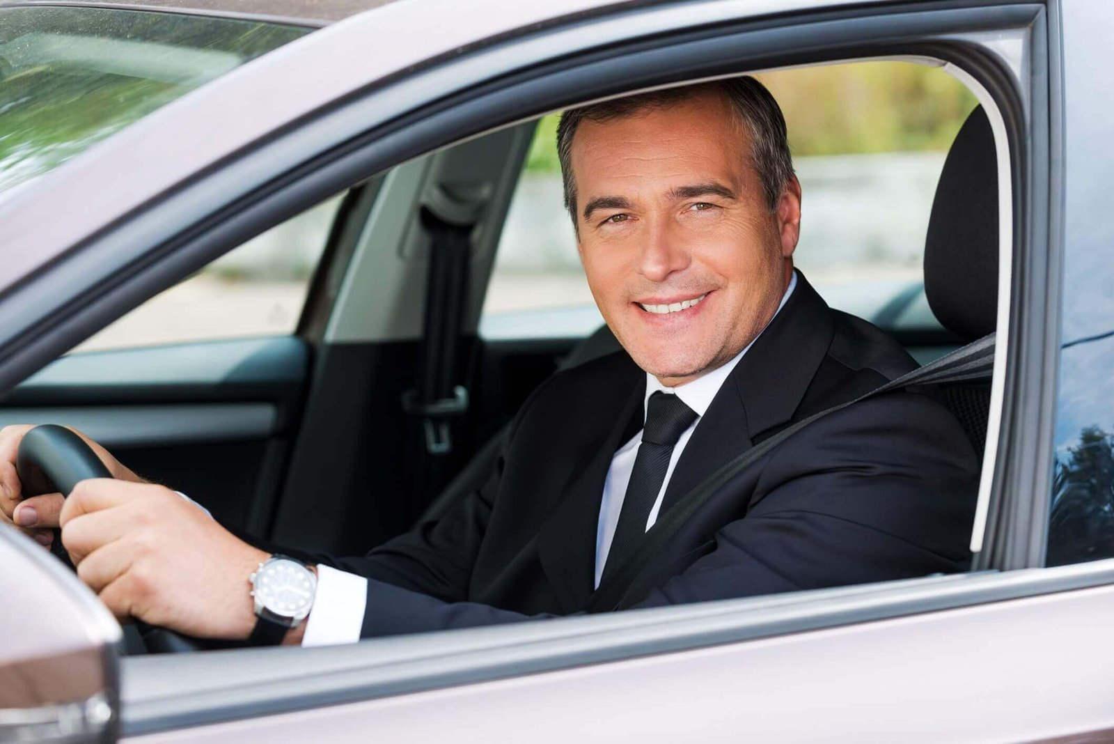 Professional chauffeur in a black suit smiling through the open driver side window